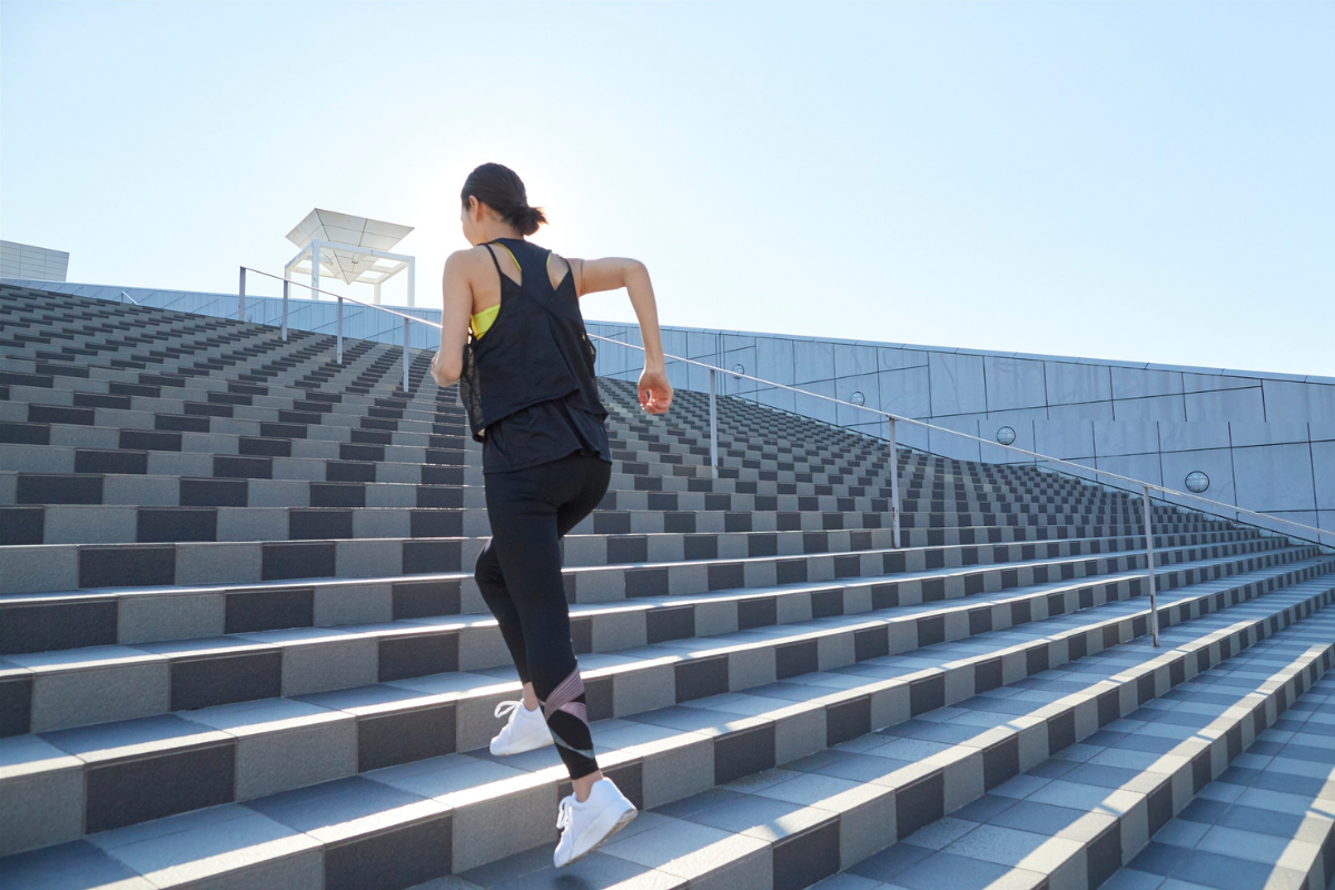 Žena v športovom oblečení beží nahor po širokých schodoch. 