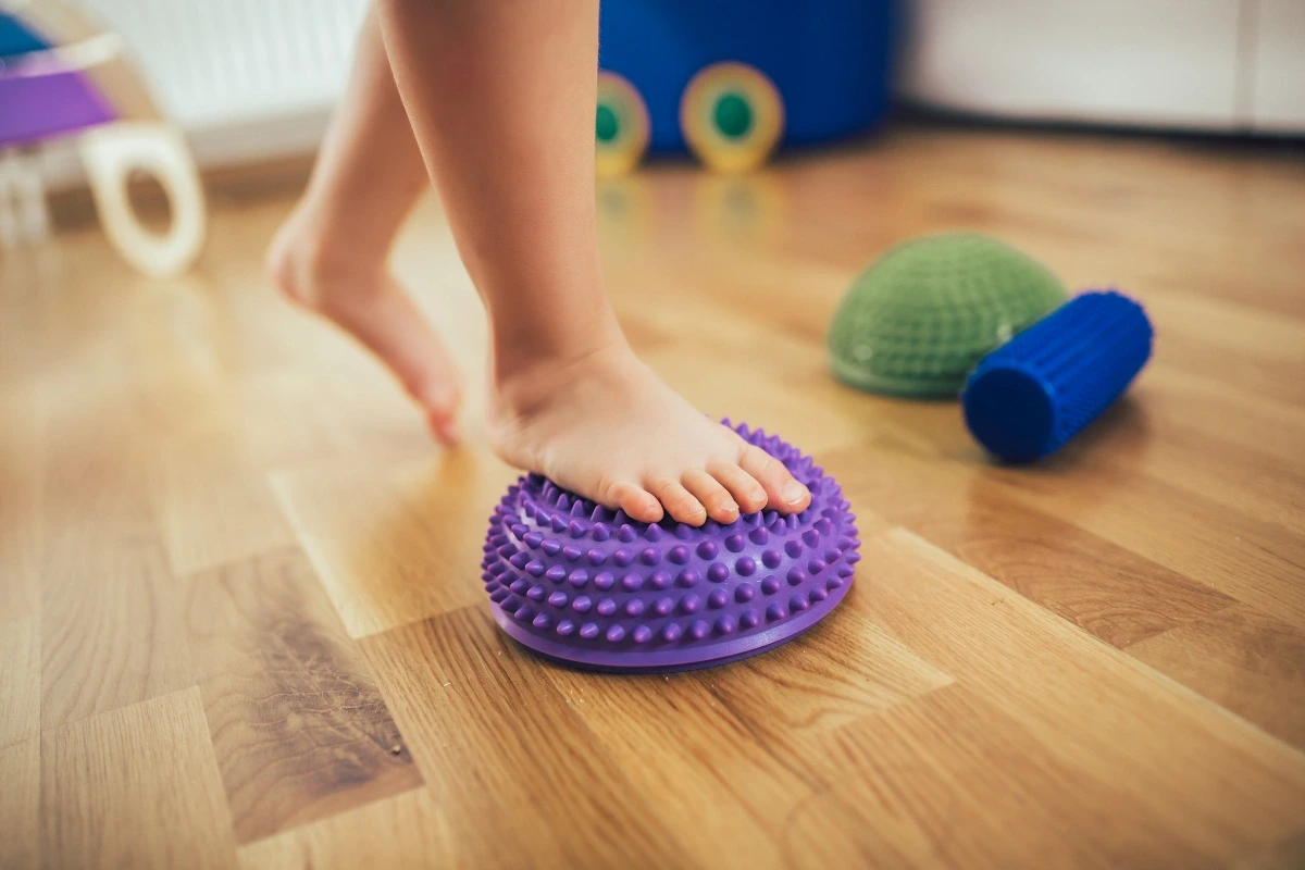 Detská noha šliapajúca naboso na fialovú masážnu pomôcku.