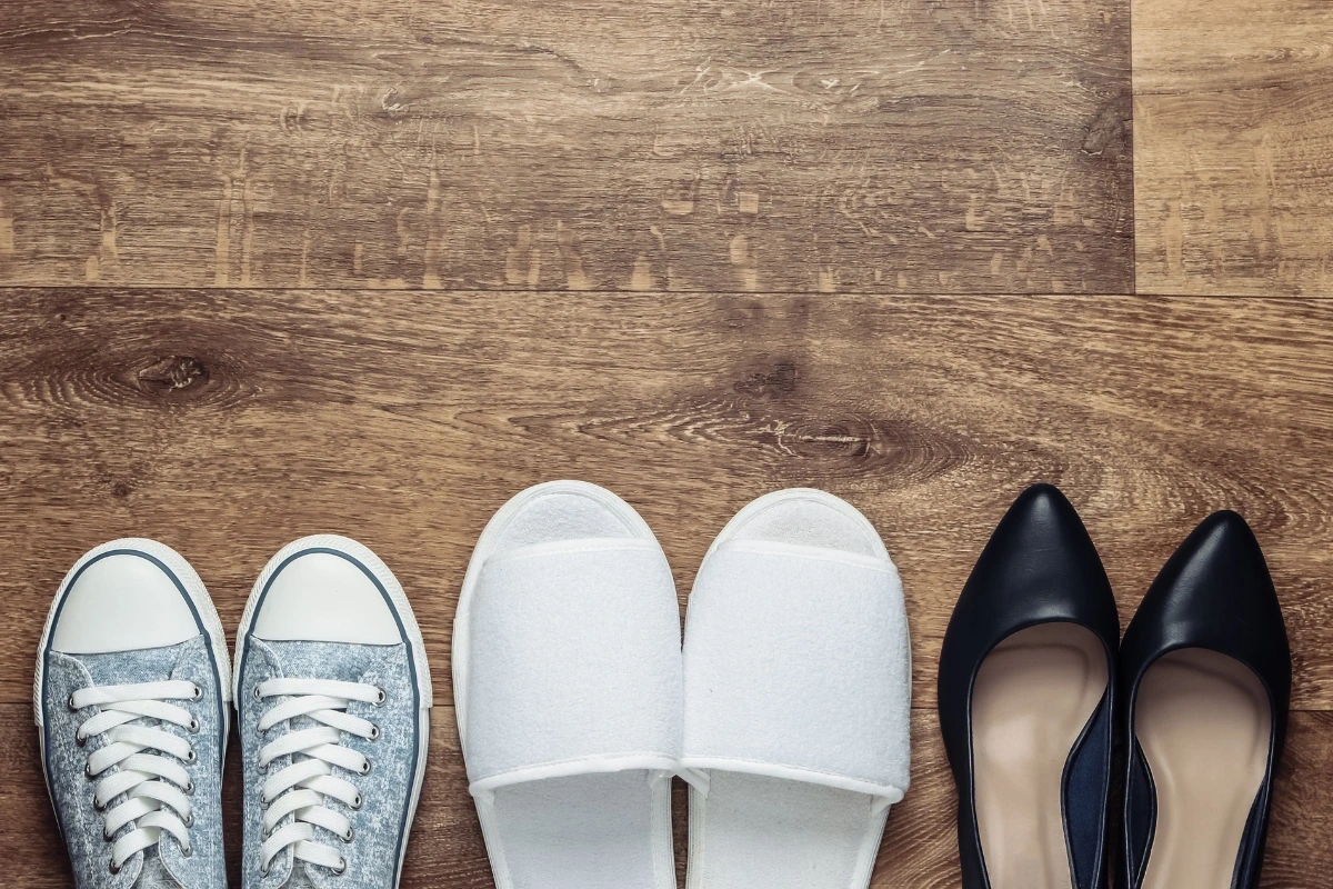 Pohľad zhora na tri rôzne páry topánok (tenisky, biele papuče, čierne lodičky).