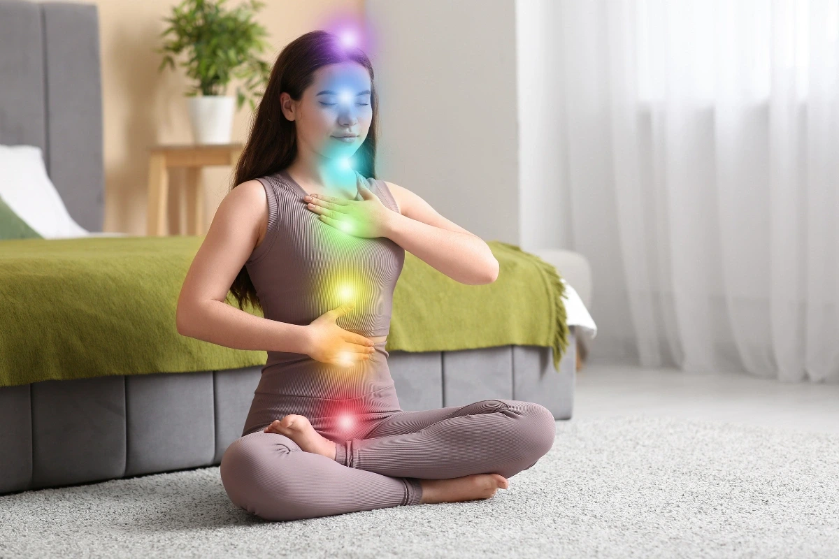 Žena v meditačnej pozícii s farebnými svetelnými bodmi na tele, ktoré predstavujú čakry.