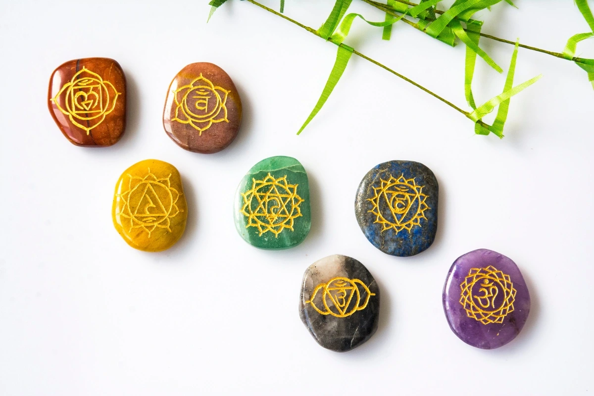 Sedem polodrahokamov s vyrytými symbolmi čakier položených na bielom podklade.