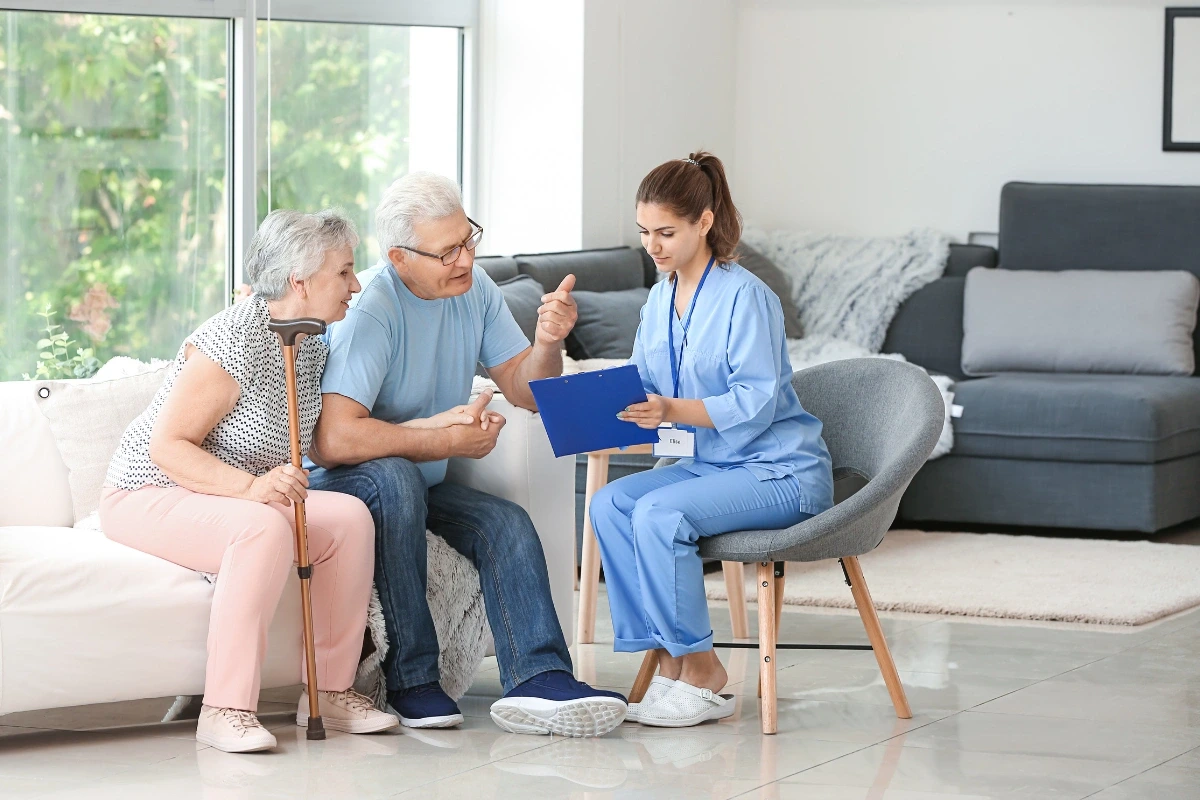 Dvojica seniorov počúva inštrukcie, ktoré im dáva zdravotná pracovníčka.