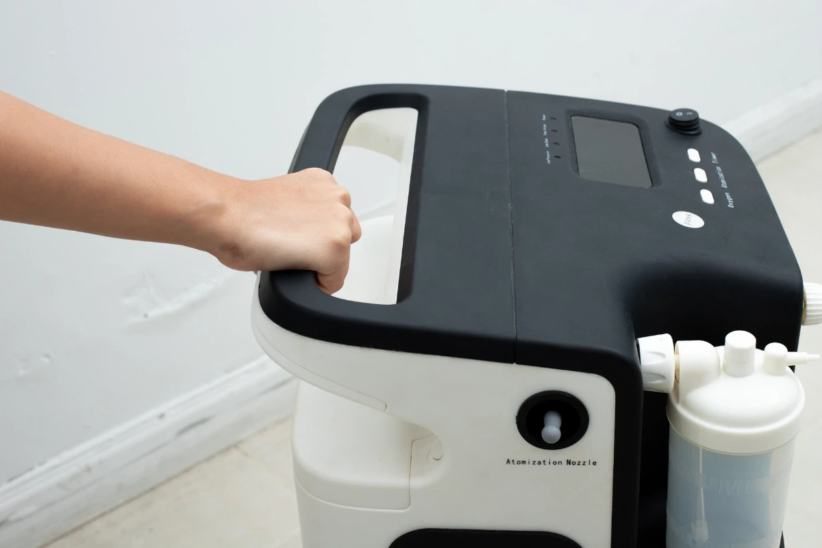 Detailný záber na ruku držiacu rukoväť prenosného kyslíkového koncentrátora.