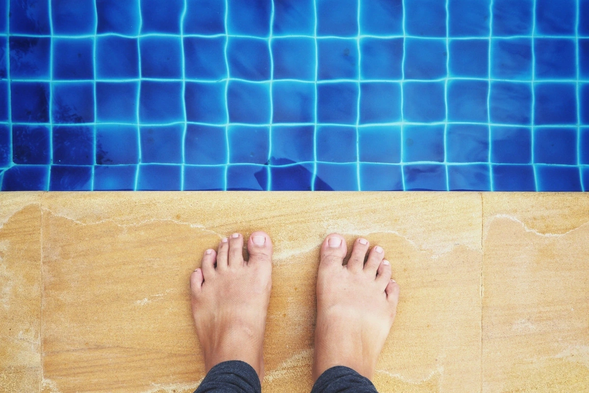 Bosé nohy stojace na dlaždiciach pri okraji bazéna.