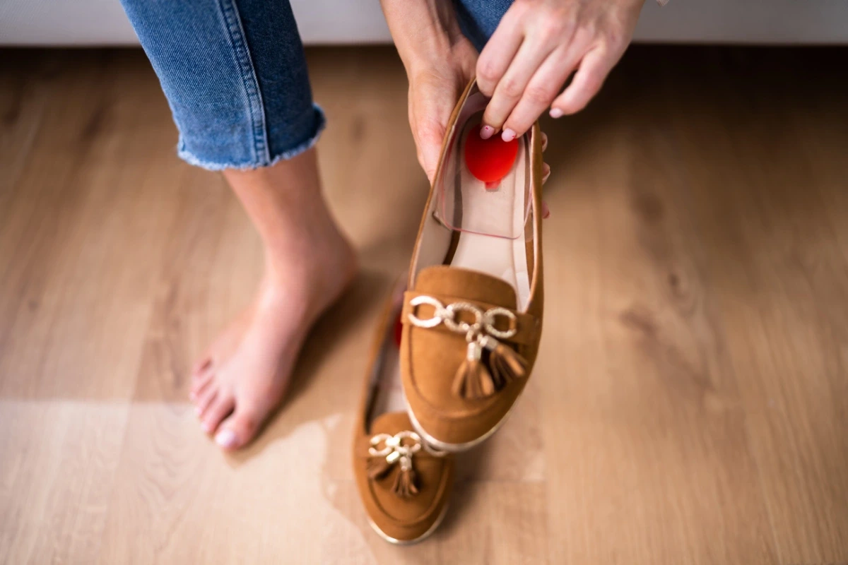 Žena vkladá gélovú podpätenku do elegantnej hnedej topánky.
