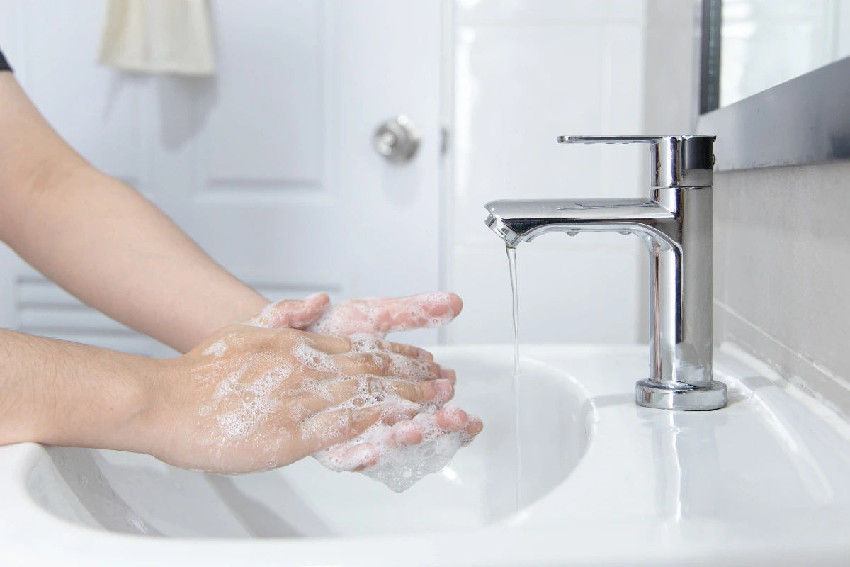 Záber na namydlené rukyy, ktoré si človek umýva pod tečúcou vodou.
