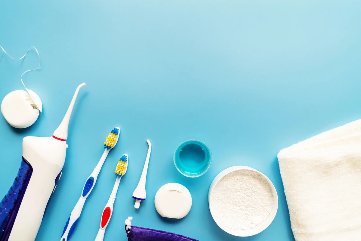 Rôzne pomôcky na dentálnu hygienu položené na svetlomodrom pozadí.