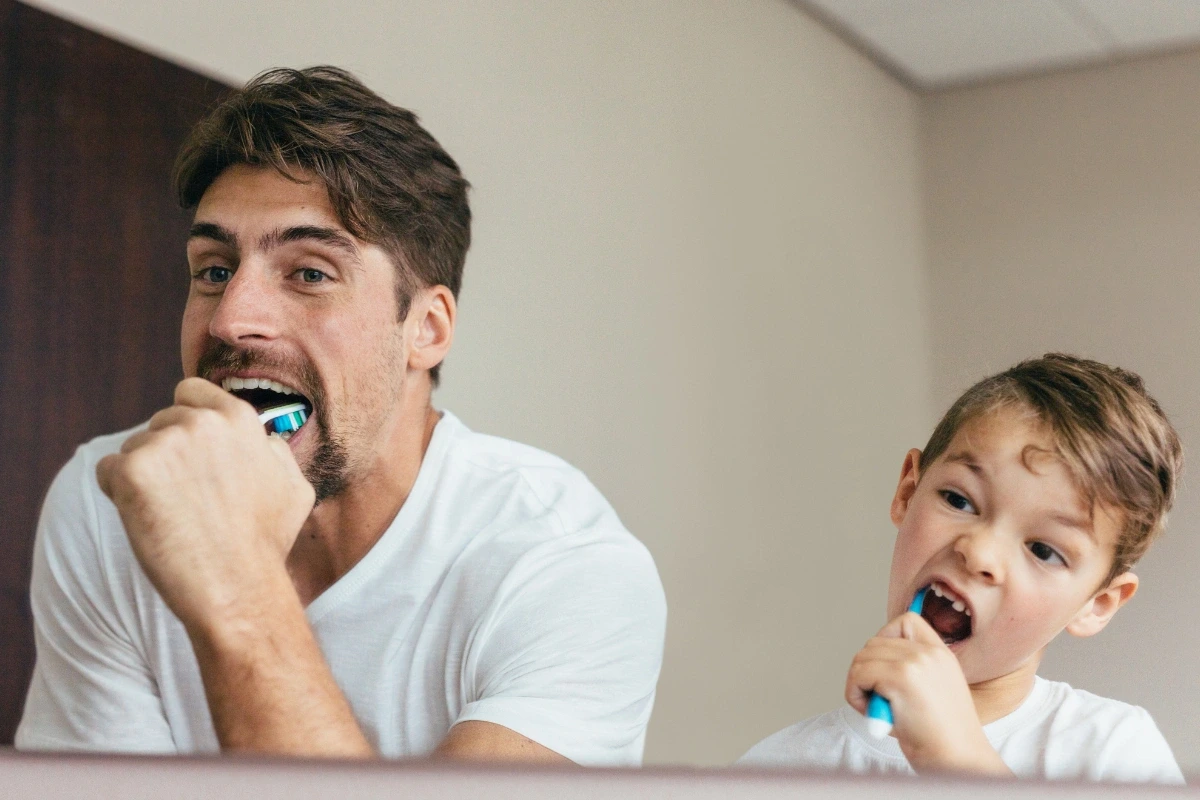 Muž a chlapec si spolu umývajú zuby pred zrkadlom v kúpeľni.