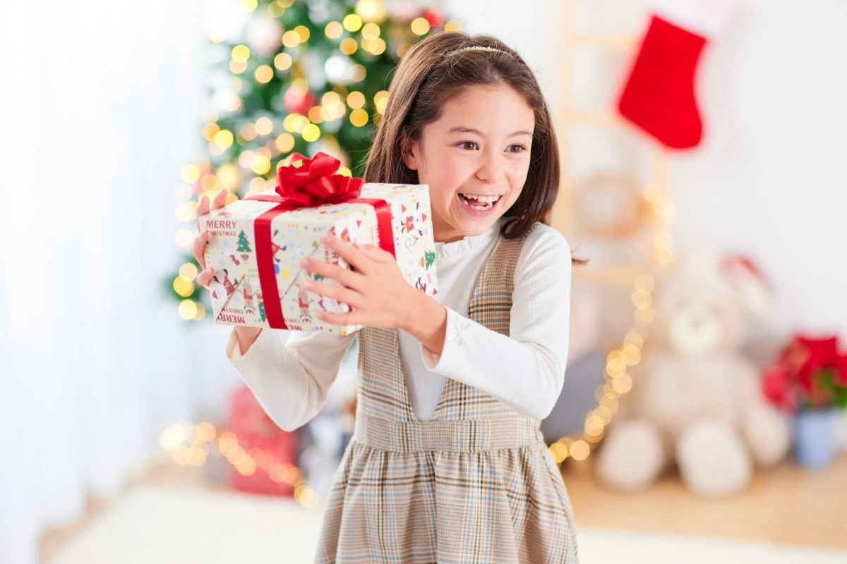 Malé dievča sa usmieva a v rukách drží zabalený vianočný darček. 
