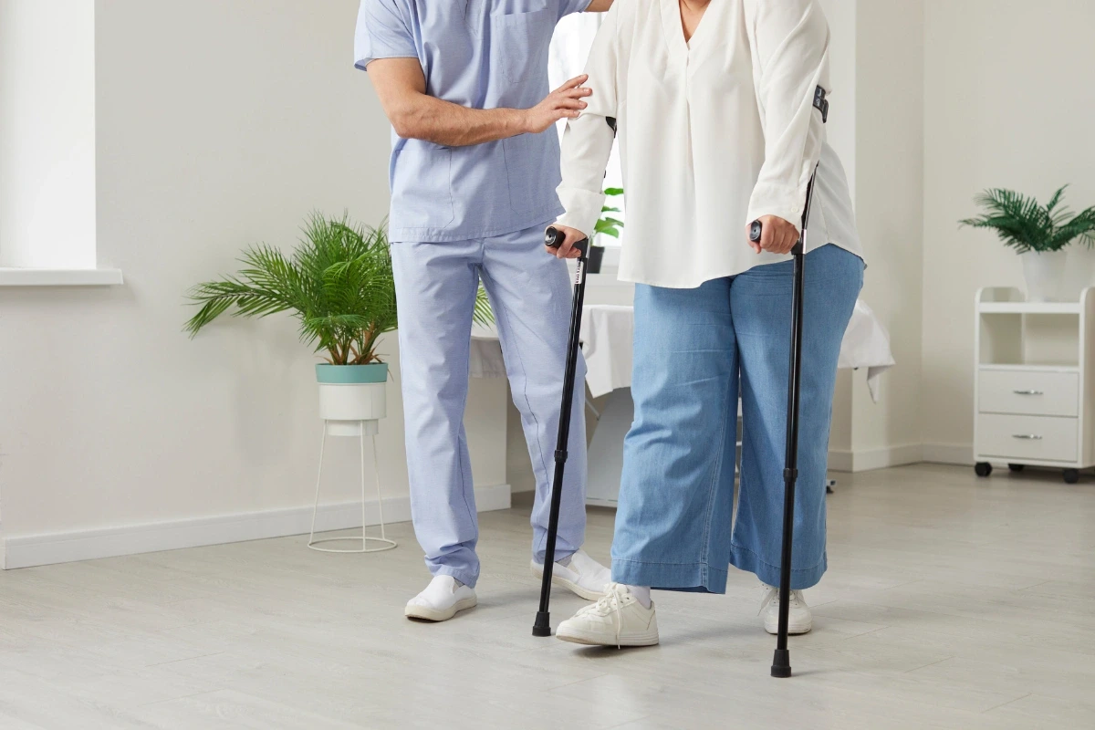 Pacientka s francúzskymi barlami za asistencie zdravotníka.