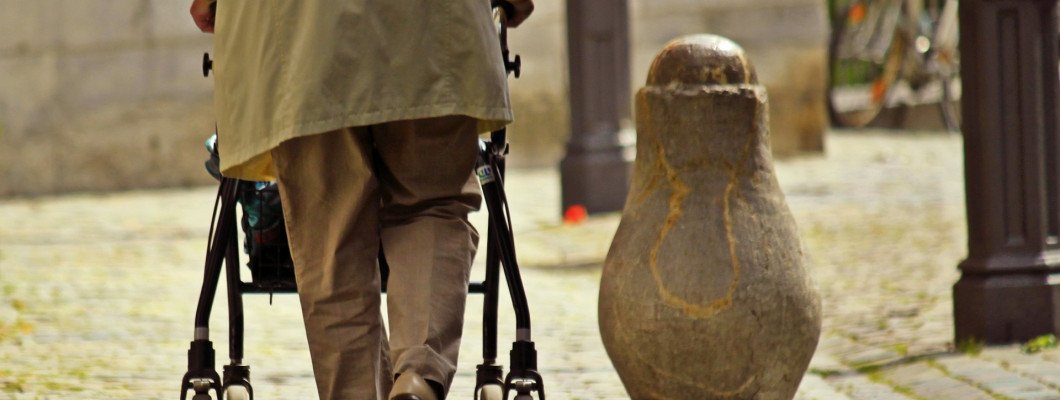 Starší muž pri chôdzi so 4-kolesovým chodítkom.